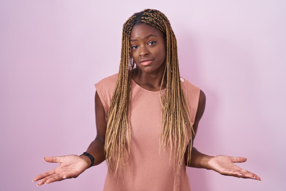 African american woman with braided hair standing over pink background clueless and confused with open arms, no idea concept.